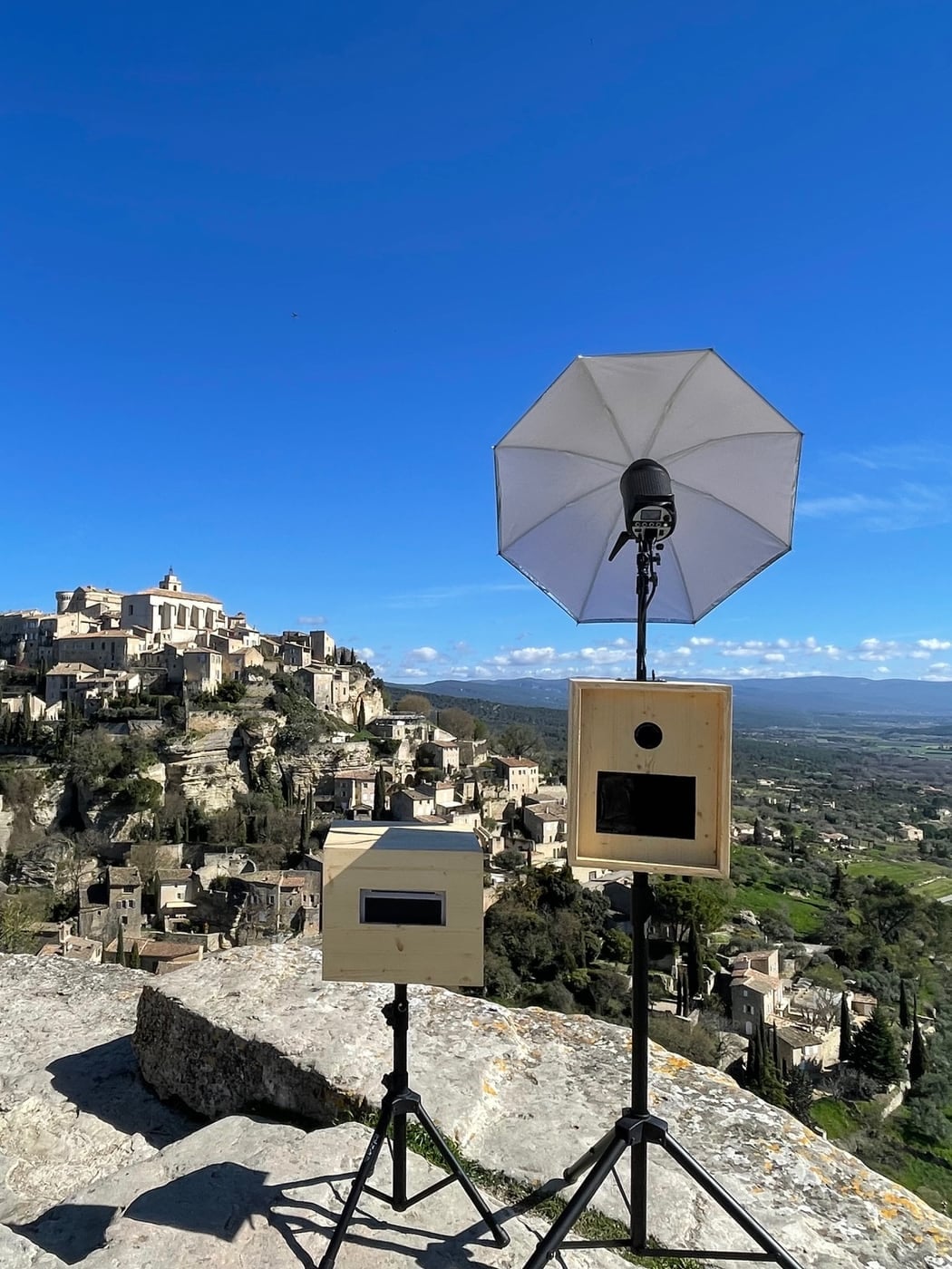 La borne photobooth Provence Photobooth avec son flash parapluie, installée face à un village perché de Provence